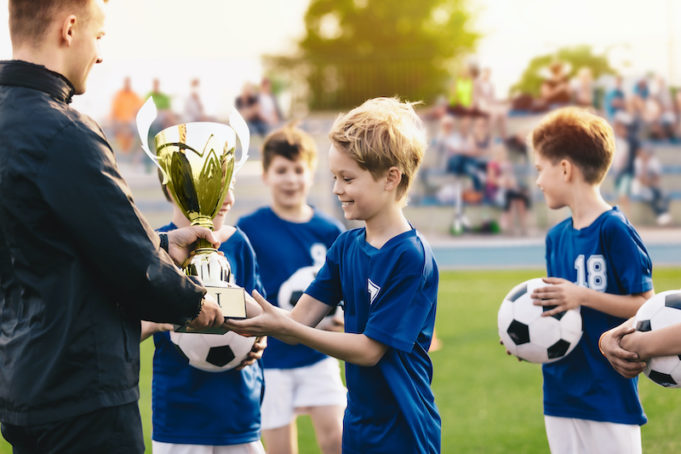 Happy Smiling Young Boys Celebrating Sports Soccer Football Championship. Team Winning Football Tournament for Youth. Sport Background. Young Soccer Player Holding Trophy. Junior Coach Hand Golden Cup