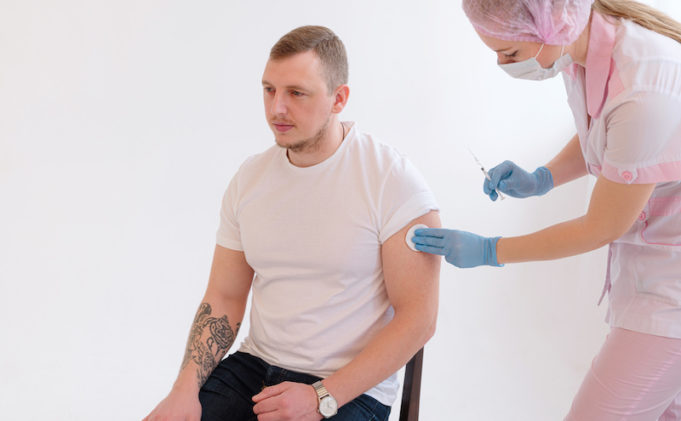 FEMale doctor holding syringe making covid 19 vaccination injection dose in shoulder of male patient.