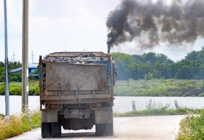 A loaded truck ride on the road with thick black smoke from the exhaust