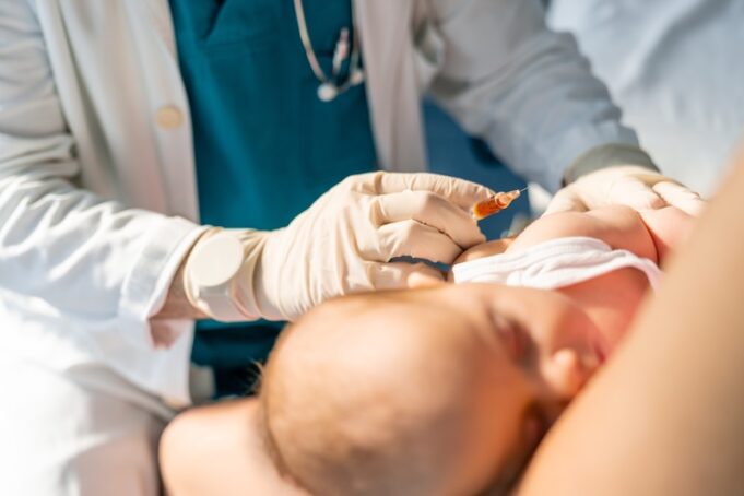 Unidentified doctor wearing protective gloves giving injection to newborn in hospital. Medical professional carefully administers an immunization to a young baby during an appointment.