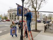 Council Member Ken Rothwell puts up a banner for Riverhead Medal of Honor recipient PFC Garfield Langhorn on Main Street, alongside a banner for Tech. Sgt. Dashan Briggs. RiverheadLOCAL/Emil Breitenbach Jr.
