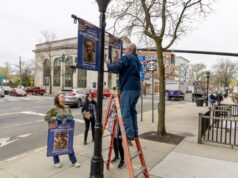 Council Member Ken Rothwell puts up a banner for Riverhead Medal of Honor recipient PFC Garfield Langhorn on Main Street, alongside a banner for Tech. Sgt. Dashan Briggs. RiverheadLOCAL/Emil Breitenbach Jr.