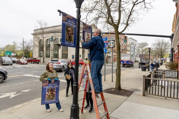 2026_0418_hometown hero banners - 1 Council Member Ken Rothwell puts up a banner for Riverhead Medal of Honor recipient PFC Garfield Langhorn on Main Street, alongside a banner for Tech. Sgt. Dashan Briggs. RiverheadLOCAL/Emil Breitenbach Jr.